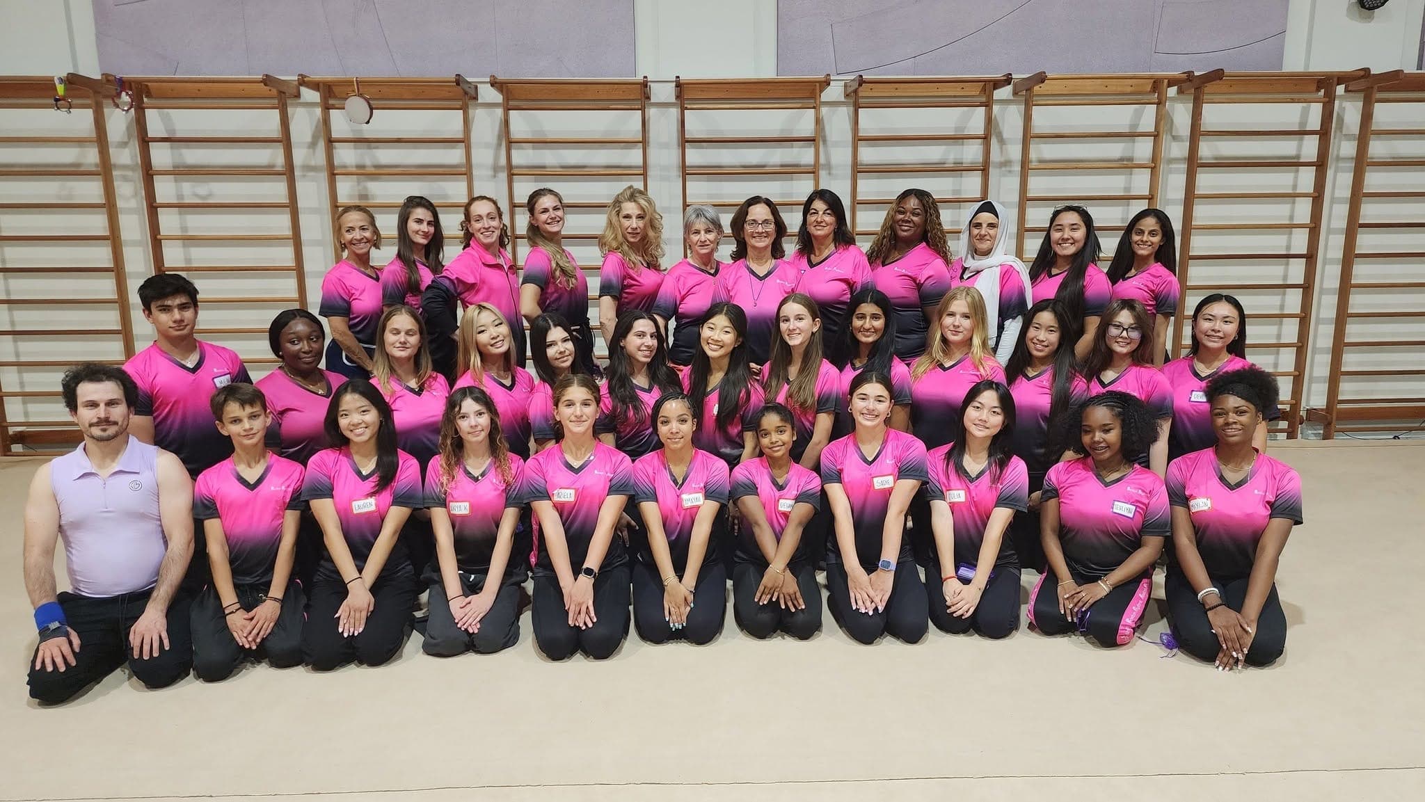 The full Boston Rhythmic team of coaches, instructors, and administrators in matching pink team jerseys