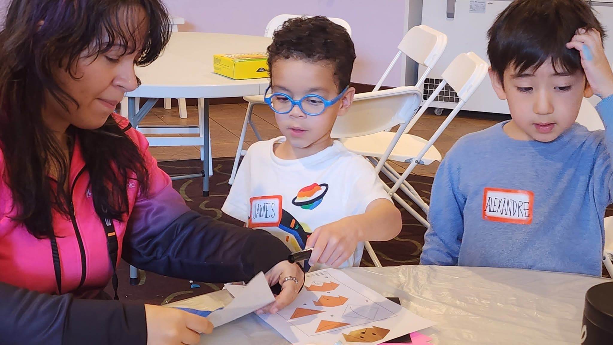 A camp coach helping two young campers with a hands-on craft project at a table